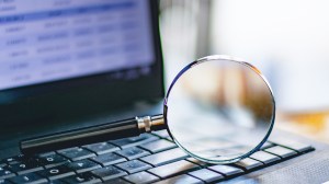 Magnifying glass set across an open laptop with data on screen